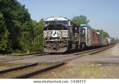 Hot summer day - view of freight train barreling down the tracks towards a road crossing.