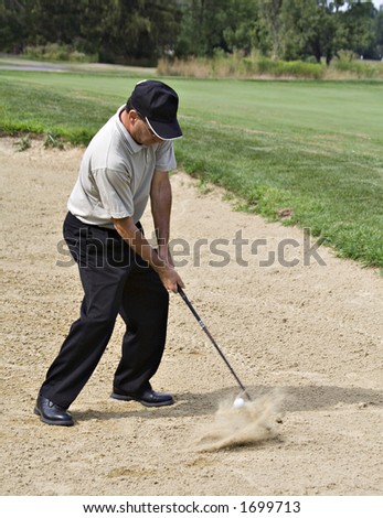 Pro driving the ball from sand trap - ball visible, hovering inches from the club and sand splash