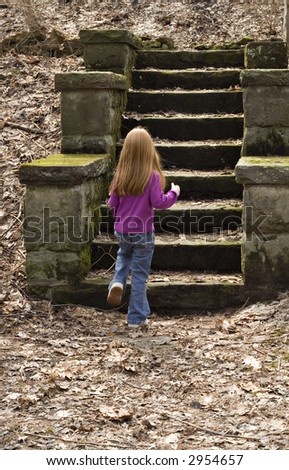 Small red-haired girl climbing stone steps in a park.