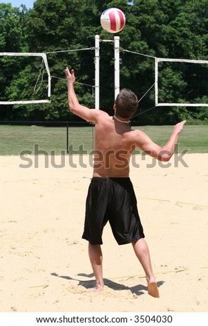 Young college man  gets ready to spike the volleyball - plays game with park during summer break.