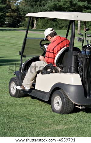 Male golfer sits in cart records his score on score card.