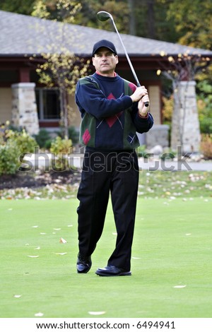 Male golfer tees of  in front of club house on an autumn day.