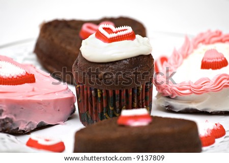 A plate of individual heart shape cakes and cupcakes decorated for valentine's day or other special occasion.