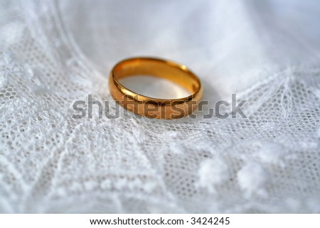 Close up of single white wedding band on white lace background