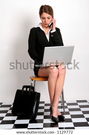 Pretty young woman in business attire talking on her cell phone and typing on her laptop computer