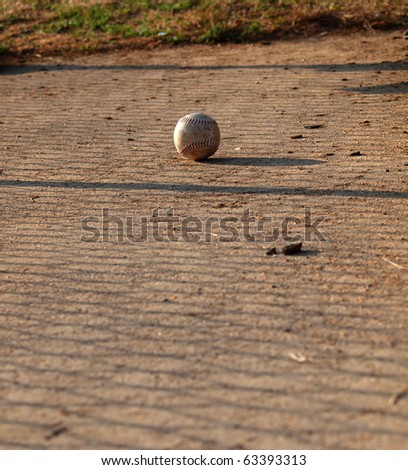 A softball in the dirt near sunset.