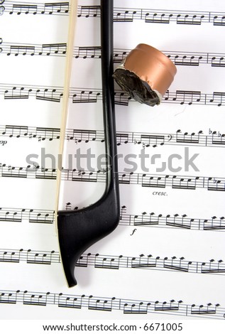 A black carbon fiber double bass bow and rosin on a piece of sheet music.
