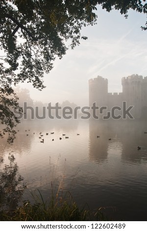 Beautiful medieval castle and moat at sunrise with mist over moat and sunlight behind castle
