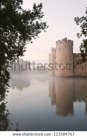 Beautiful medieval castle and moat at sunrise with mist over moat and sunlight behind castle