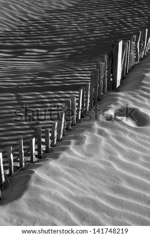 Wooden fence in sand dunes with strong shadows from sunlight