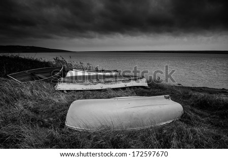 Old abandoned rowing boats on shore of lake with stormy sky overhead