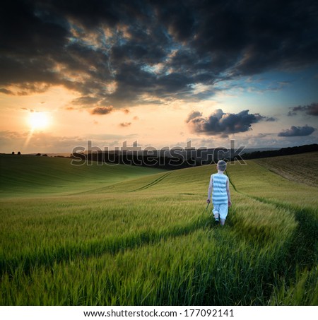Landscape young boy walking through crop field at sunset