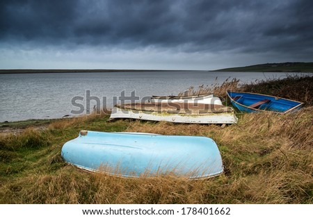 Old abandoned rowing boats on shore of lake with stormy sky overhead