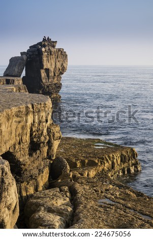 Rocky cliff landscape with sunset over ocean with unidentified people on cliff top