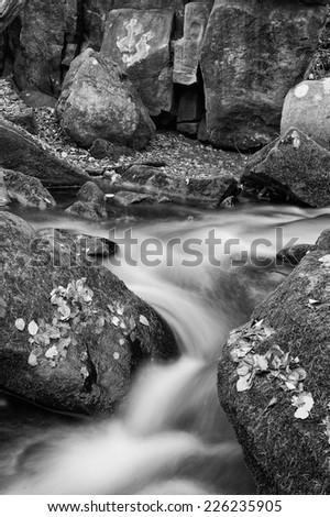 Blurred water detail with rocks and Autumn leaves in Padley Gorge in Peak District  black and white