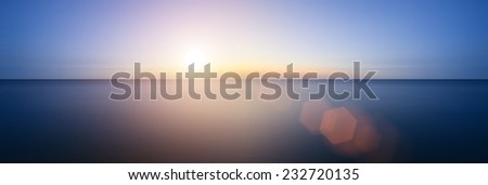 Conceptual image of sunrise sunset with added lens flare over still water ocean