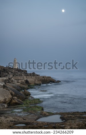Rocky cliff landscape with moon over ocean