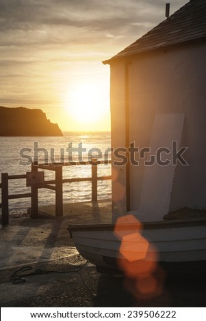 Beautiful sunrise behind fishing hut in Lulworth Cove with added lens flare