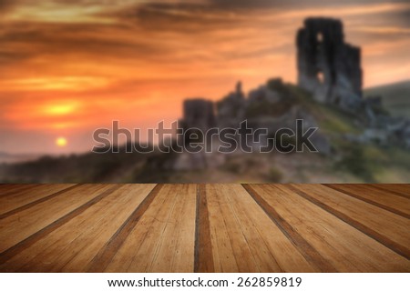 Landscape with castle ruins on hill and vibrant beautiful sunrise in distance with wooden planks floor