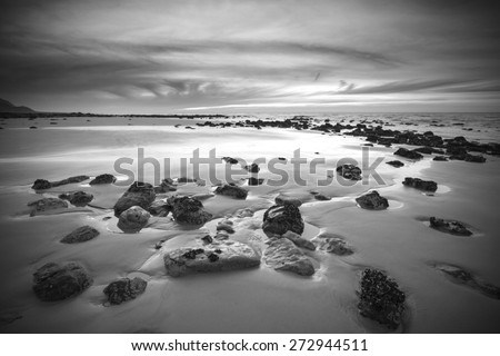 Sunrise landscape on rocky sandy beach with vibrant sky and clouds in black and white