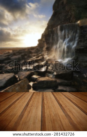 Beautiful landscape waterfall flowing into rocks on beach at sunset with wooden planks floor