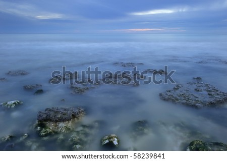Smooth long exposure motion blur sea over low rocks in water