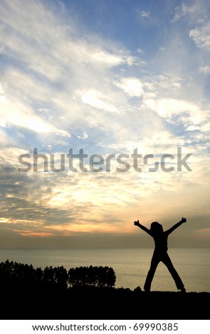 Silhouette of young happy girl looking out to sea with arms stretched in victory pose