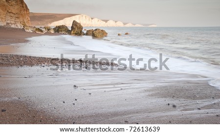Seascape of receding waves with rocks in foreground and white cliffs in distance
