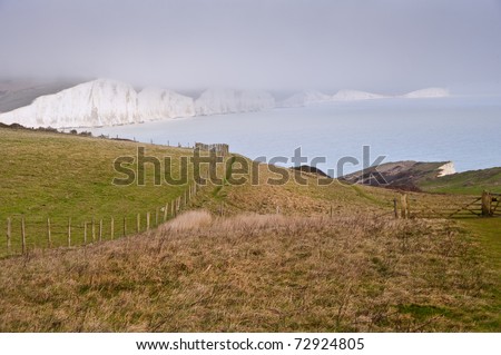 View across cliff top towards white cliffs in distance with sea in middle ground