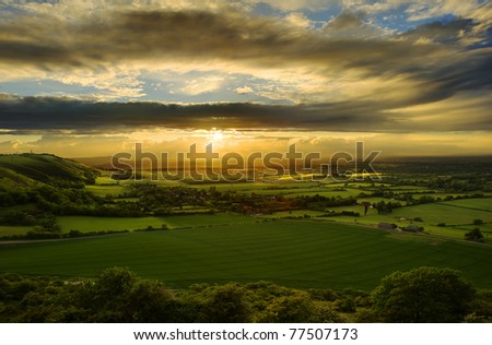 Beautiful sunset over countryside landscape of rolling hills with sun beams piercing sky and lighting hillside