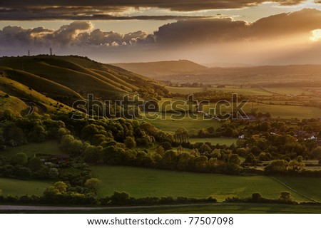 Beautiful sunset over countryside landscape of rolling hills with sun beams piercing sky and lighting hillside