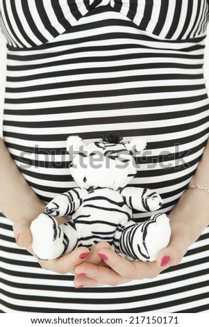 Belly of pregnant woman in stripped dress with zebra toy