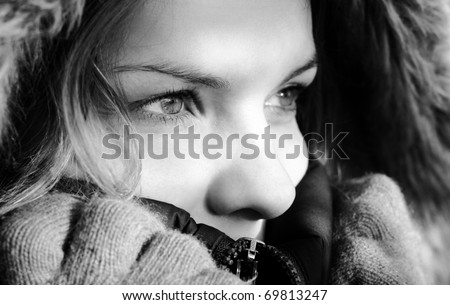 Black and white photo of beautiful young woman wearing winter jacket hood and gloves