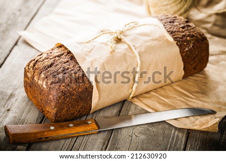 Traditional bread with seeds wrapped in paper on old wooden table