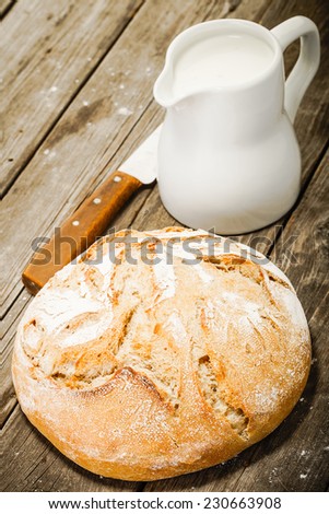 white bread, ceramic jug with milk and knife on old vintage wooden table
