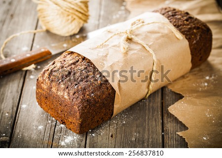 Traditional bread with seeds wrapped in paper on old wooden table