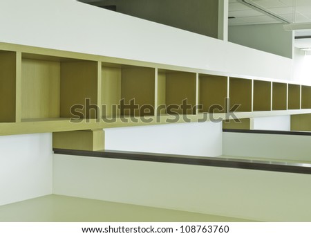 Long empty wooden bookshelf with dividers above office cubicles