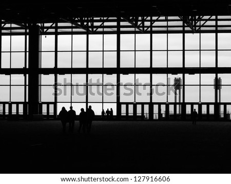 Eight unidentifiable adults in silhouette by closed doors and large windows of dark hall in convention center, in black and white