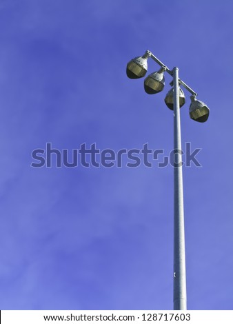 Row of four stadium lights atop metal pole on a sunny afternoon