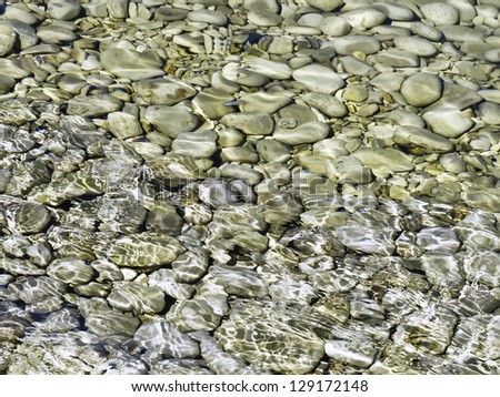 Half and half at the beach: Smooth stones in shallow water shimmer in sunlight while the rest bake dry