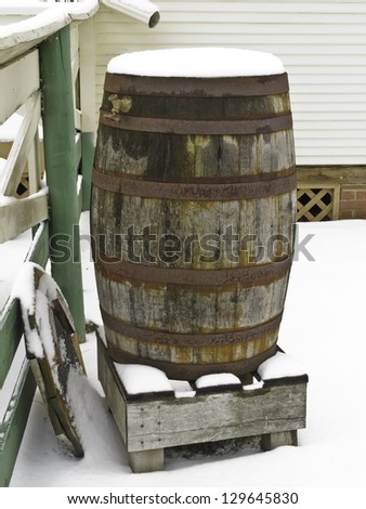 Winter on the farm: Weathered old barrel cistern with brass spigot and rusty iron hoops on wooden stand in snow, northern Illinois