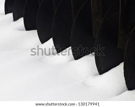 Winter on a farm: Row of circular blades of vintage tiller in snow