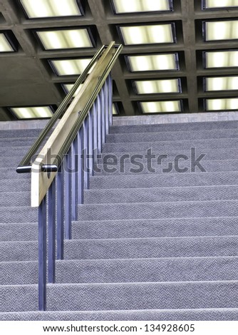 On your way to the top: Handrail above carpeted stairway with fluorescent lights overhead (selective focus)