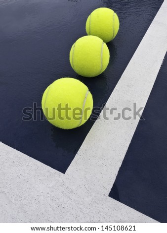 Three yellow tennis balls in corner of outdoor tennis court after rain