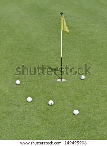 Five striped practice golf balls near hole with short flag on practice green