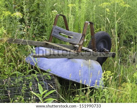 Summer vacation: Blue wheelbarrow upside down by roll of wire in garden weeds, August  in northern Illinois