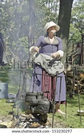 WHEATON, ILLINOIS/USA - SEPTEMBER 7: American Revolutionary War (1775-1783) reenactment on September 7, 2013, in Wheaton, IL. Woman in period dress tends a camp fire in colonial military encampment.
