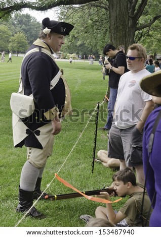 WHEATON, ILLINOIS/USA - SEPTEMBER 7: American Revolutionary War (1775-1783) reenactment on September 7, 2013, in Wheaton, IL. Actor-soldier in uniform chats with spectators by mock battlefield.