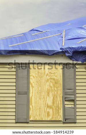 House repairs after tornado: Boarded window beneath roof with protective sheets of blue plastic