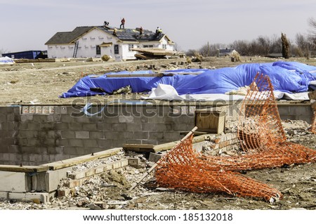 WASHINGTON, ILLINOIS, USA - MARCH 31, 2014: Foundations of a house remain exposed while roofers repair a neighbor's house after a tornado devastated entire neighborhoods here on November 17, 2013.